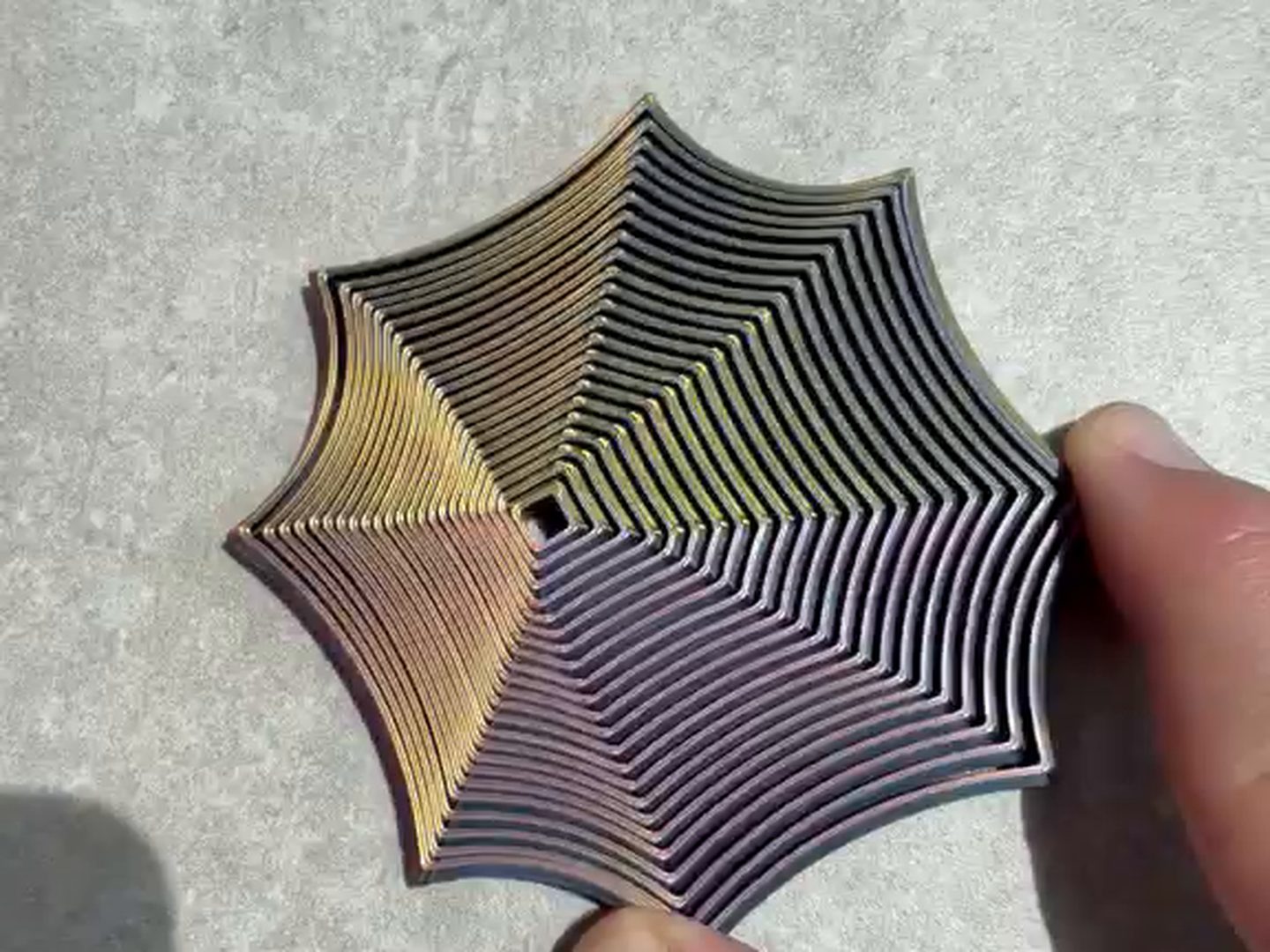 A Focus Spiral focus toy open flat in an adult hand, gold through purple